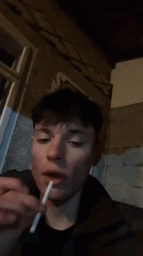 A Person Is Smoking A Cigarette In Front Of A Wall With A Floral Design On It GIF