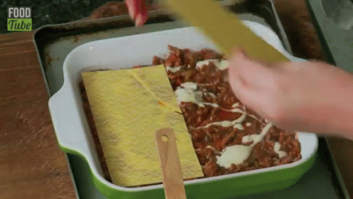 A Person Is Spreading Cheese On Top Of A Casserole Dish With Food Tube Written On The Bottom . GIF