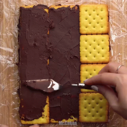 A Person Is Spreading Chocolate Icing On Crackers With The Words Mr.cakes Visible GIF