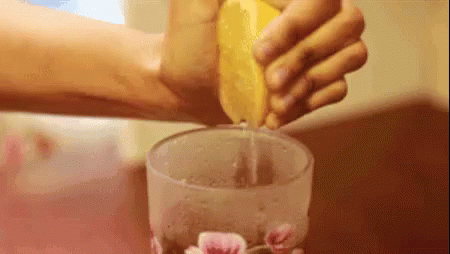 A Person Is Squeezing Lemon Juice Into A Glass . GIF