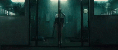 A Person Is Standing In A Dark Room Behind A Glass Door Holding A Knife . GIF