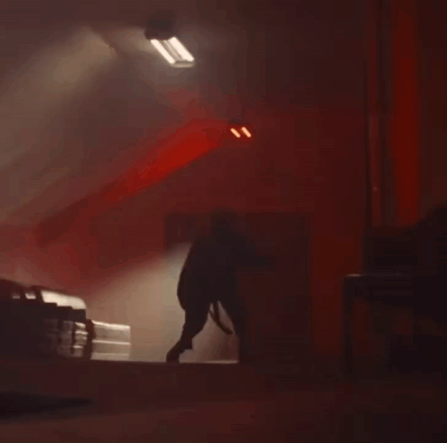A Person Is Standing In A Dark Room With A Red Light On The Ceiling . GIF