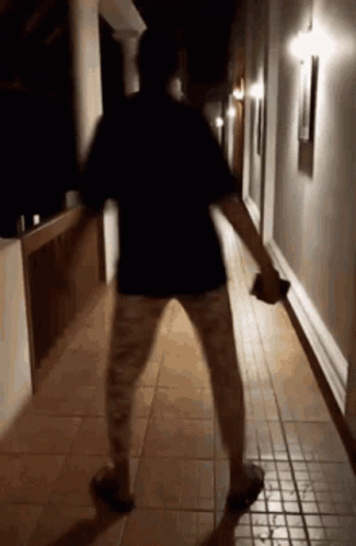 A Person Is Standing In A Hallway At Night Holding A Bottle . GIF
