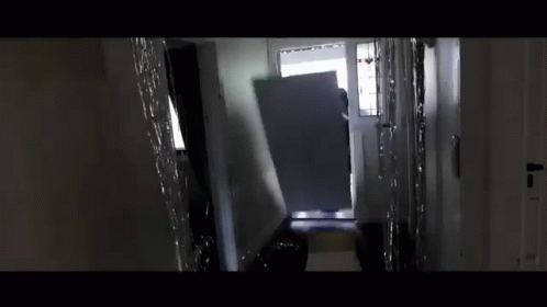 A Person Is Standing In A Hallway Carrying A Large Piece Of Furniture . GIF
