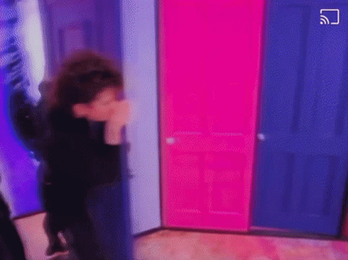 A Person Is Standing In A Room With Pink And Blue Doors And Covering Their Face . GIF