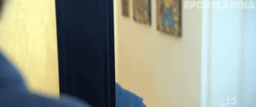 A Person Is Standing In Front Of A Door With A Painting On The Wall Behind Them . GIF