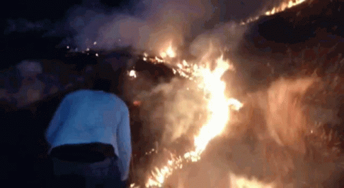 A Person Is Standing In Front Of A Fire At Night . GIF