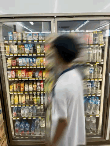 A Person Is Standing In Front Of A Refrigerator In A Store GIF