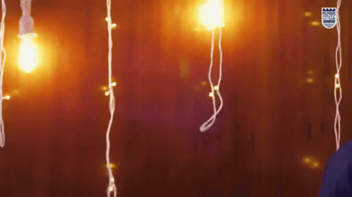 A Person Is Standing In Front Of A Wall With Christmas Lights Hanging From It GIF