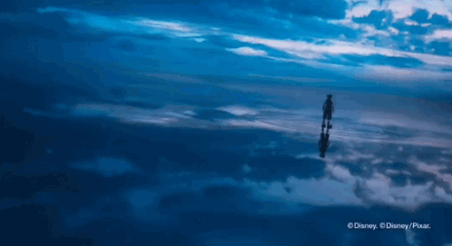A Person Is Standing In The Middle Of A Cloudy Sky And Their Reflection Is In The Clouds GIF