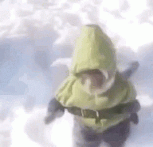 A Person Is Standing In The Snow Wearing A Yellow Hooded Jacket And Goggles . GIF
