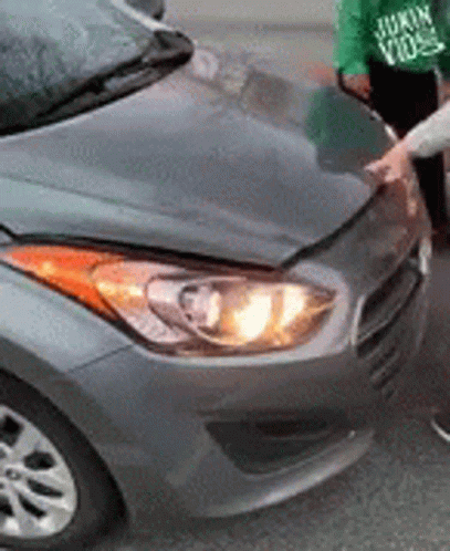A Person Is Standing Next To A Gray Car With The Hood Up . GIF