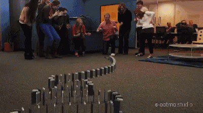 A Person Is Standing Next To A Row Of Dominoes In A Hallway . GIF