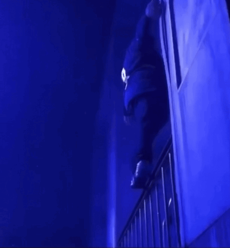 A Person Is Standing On A Railing In A Dark Room With Blue Lights GIF