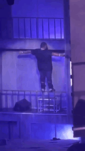 A Person Is Standing On A Stage With Their Arms Outstretched In A Dark Room GIF