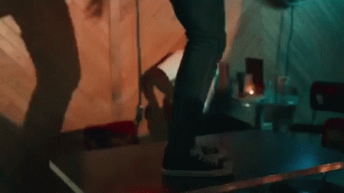 A Person Is Standing On A Table In A Dark Room With A Shadow On The Wall . GIF