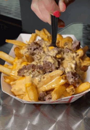 A Person Is Taking A Bite Of French Fries With Cheese GIF