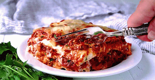A Person Is Taking A Bite Of Lasagna With A Silver Fork GIF