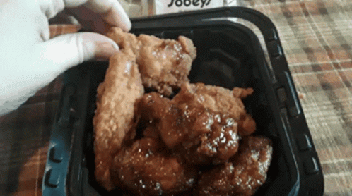 A Person Is Taking A Piece Of Fried Chicken Out Of A Container GIF