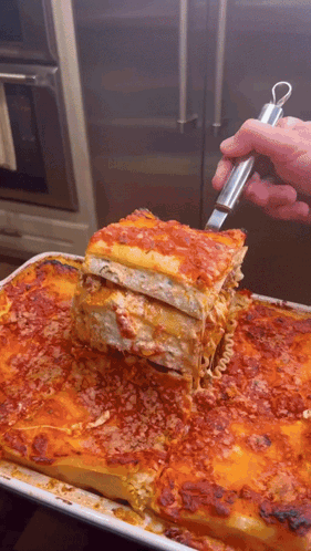 A Person Is Taking A Slice Of Lasagna From A Pan GIF