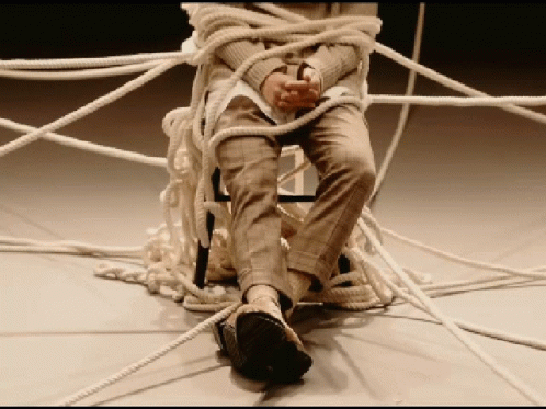 A Person Is Tied Up With Ropes And Sitting On A Chair GIF