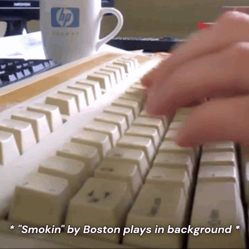 A Person Is Typing On A Keyboard With A Cup Of Coffee In The Background GIF