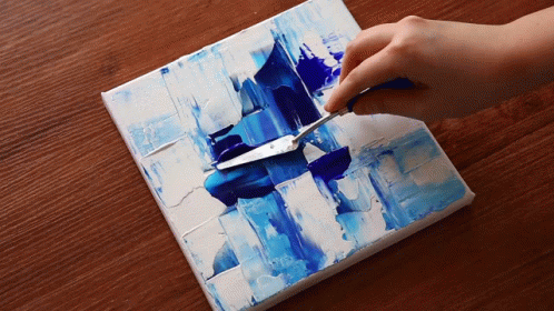 A Person Is Using A Palette Knife To Spread Blue Paint On A Canvas GIF