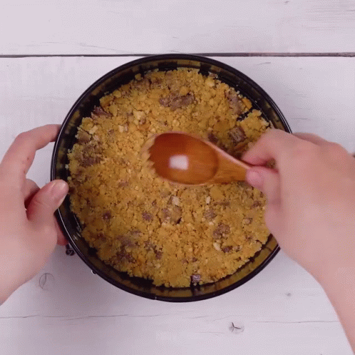 A Person Is Using A Wooden Spoon To Stir A Crumbly Crust In A Pan GIF