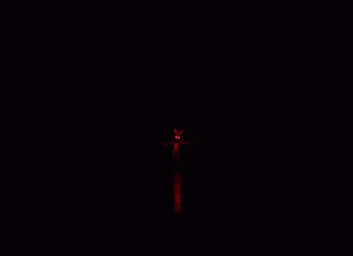 A Person Is Walking Down A Hallway With Red Lights On The Ceiling . GIF
