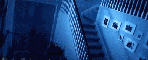 A Person Is Walking Down A Set Of Stairs In A Dark Room With Pictures On The Wall . GIF