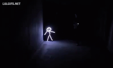A Person Is Walking Through A Dark Room With A Stick Figure Drawn On The Wall . GIF