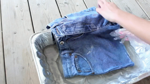 A Person Is Washing A Pair Of Jeans In A Tin Foil Tray GIF