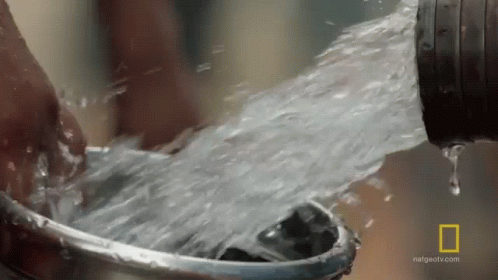 A Person Is Washing Their Hands In A Bucket Of Water From A Hose . GIF
