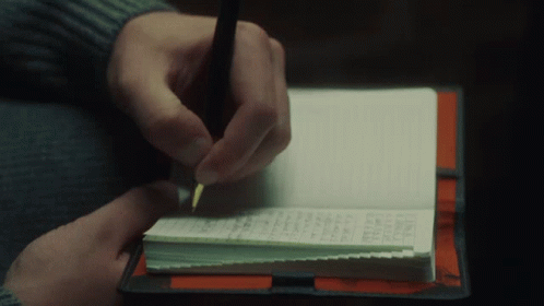 A Person Is Writing In A Notebook With A Pen On Top Of It GIF