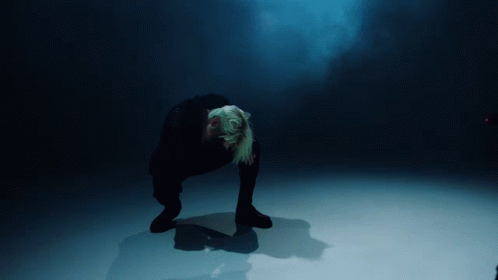 A Person Kneeling Down In A Dark Room With A Blue Light Behind Them GIF