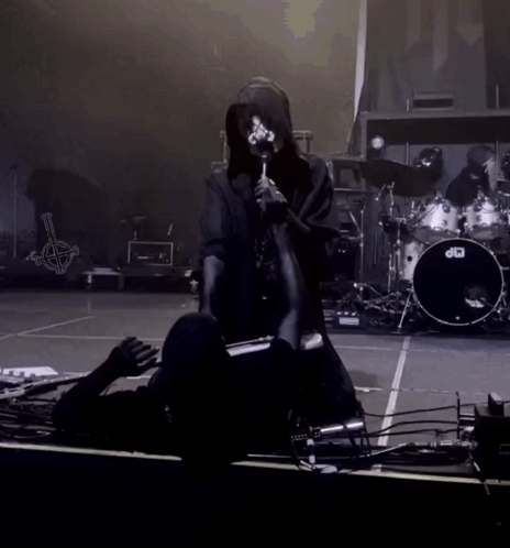 A Person Kneeling Down On A Stage With A Drum Set In The Background GIF