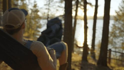 a person laying in a hammock with a backpack looking at a lake