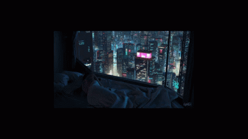 A Person Laying On A Bed Looking Out A Window At The City At Night GIF