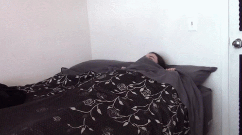 A Person Laying On A Bed With A Black And White Floral Blanket GIF