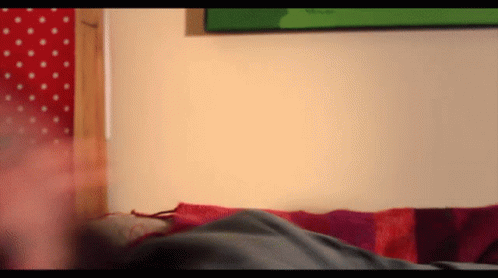 A Person Laying On A Bed With A Red And Purple Striped Blanket GIF
