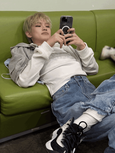 A Person Laying On A Green Couch Looking At Their Cell Phone GIF