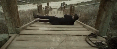 A Person Laying On A Wooden Bridge With Their Feet Up GIF