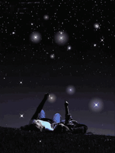 A Person Laying On The Ground Pointing At The Stars In The Night Sky GIF