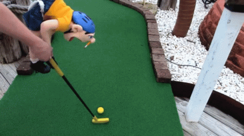 A Person Playing A Game Of Mini Golf With A Monkey Holding A Golf Club GIF