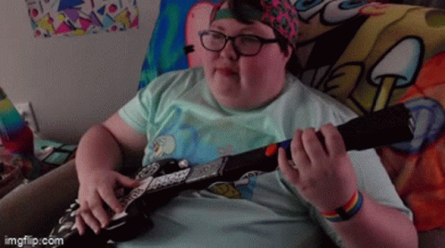 A Person Playing A Guitar With A Spongebob Blanket Behind Them GIF