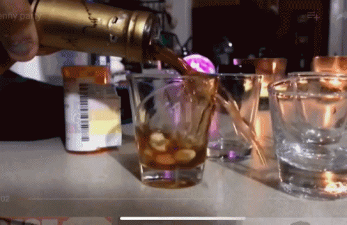 A Person Pouring A Drink Into A Shot Glass With A Pill Bottle In The Background GIF