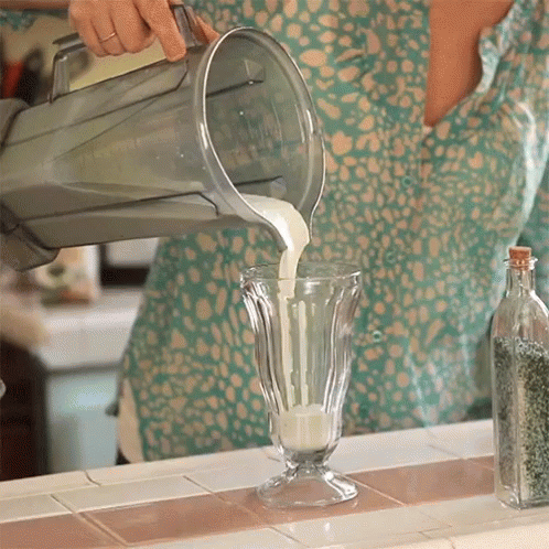 A Person Pouring Milk Into A Glass On A Counter GIF