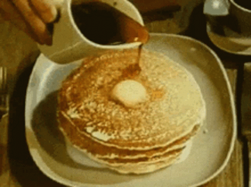 a person pouring syrup on a stack of pancakes with butter