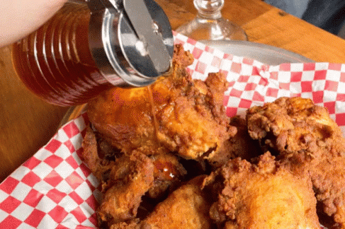 A Person Pouring Syrup Over Fried Chicken On A Checkered Napkin GIF
