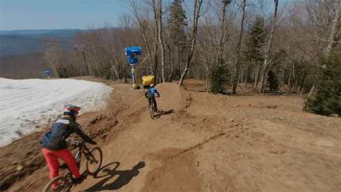 A Person Riding A Bike Down A Dirt Road With A Snow Cannon In The Background GIF